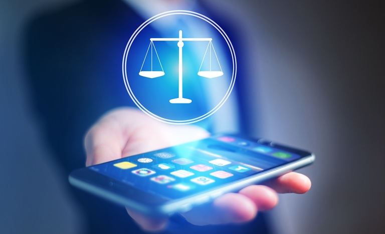 A hand holds out an illuminated phone with an array of social media icons on the screen and a projection of the scales of justice floating above it