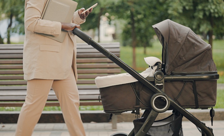 photo of a woman pushing a stroller in the city with a cellphone in her hand that she's reading