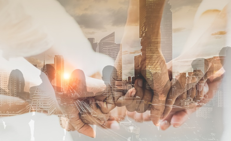 Double exposure of people holding hands over a cityscape with skyscrapers and a sunset.