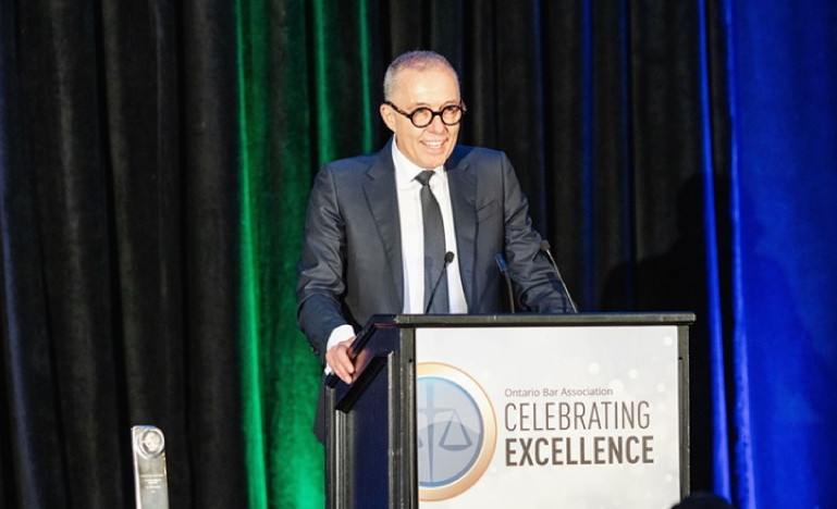 Man in a suit and glasses speaking at a podium during the Ontario Bar Association's 'Celebrating Excellence' event.
