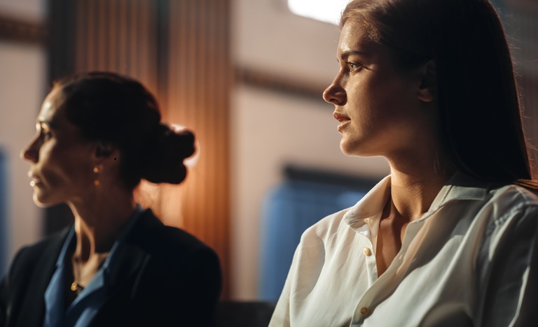 a woman seated in court next to her female attorney looking worried and fearful