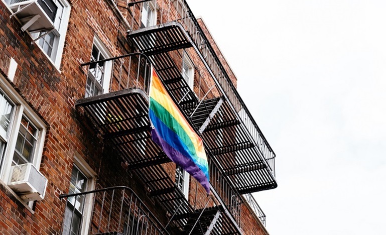 apartment building viewed from outside with PRIDE flag hanging from a window
