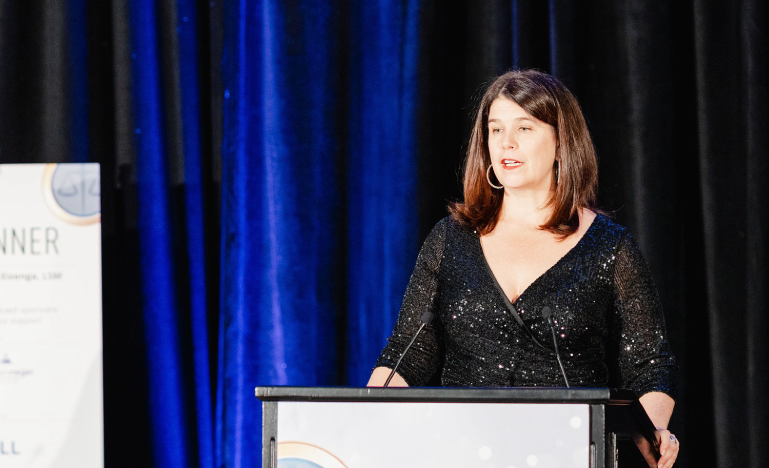 OBA President Kate Manning speaking at a podium during an Ontario Bar Association event, wearing a black sequined dress.