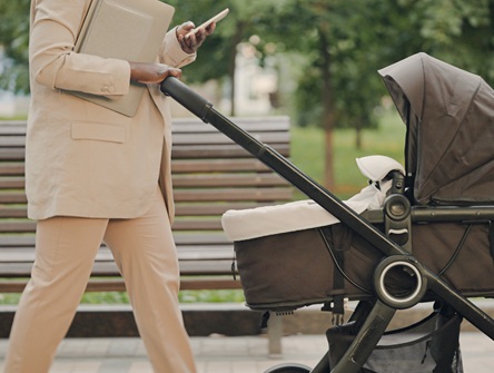 photo of a woman pushing a stroller in the city with a cellphone in her hand that she's reading