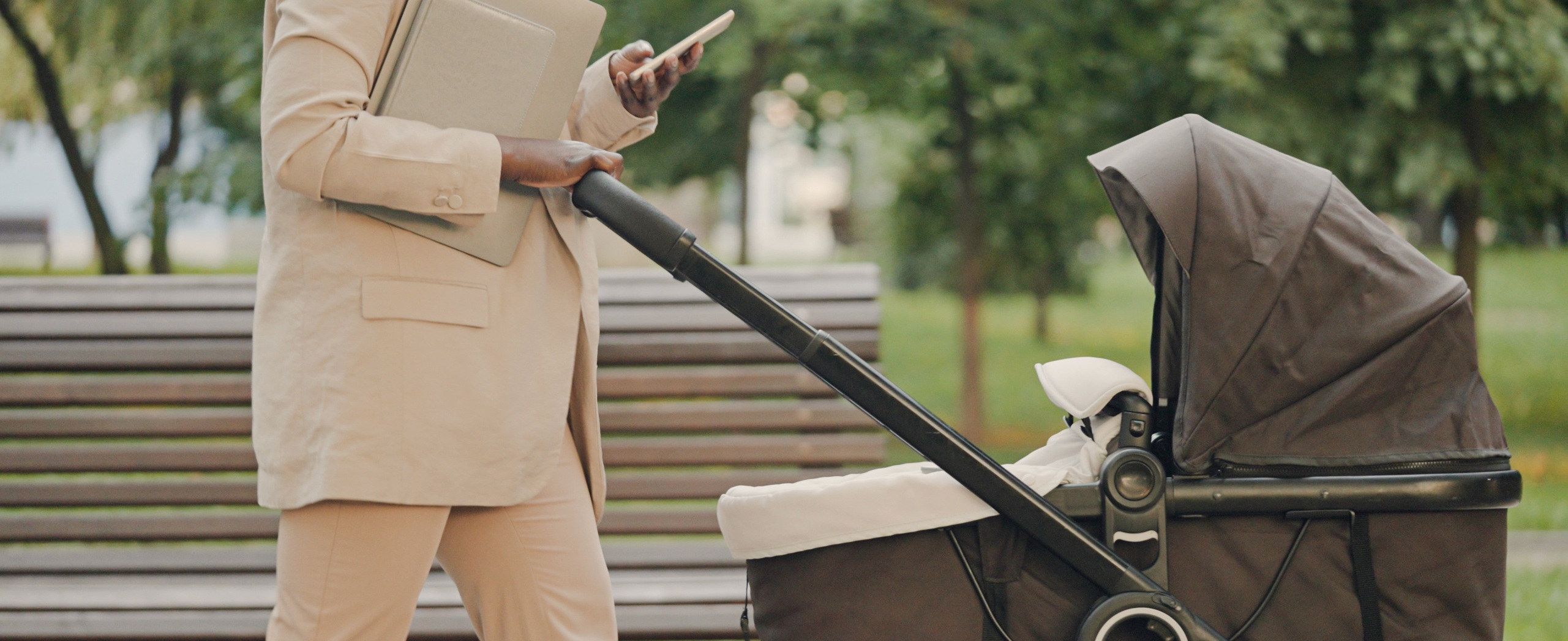 photo of a woman pushing a stroller in the city with a cellphone in her hand that she's reading