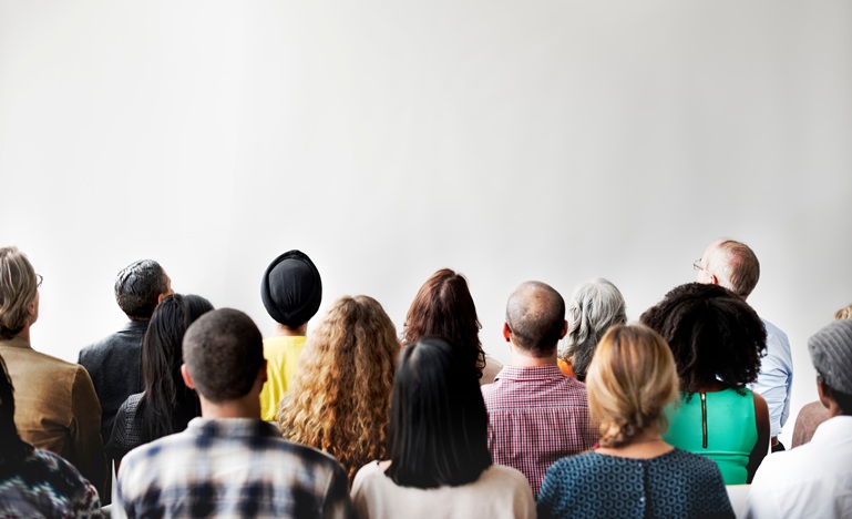 a small group of people, various ages, genders and races, stands with backs to the camera facing a blank whiteboard