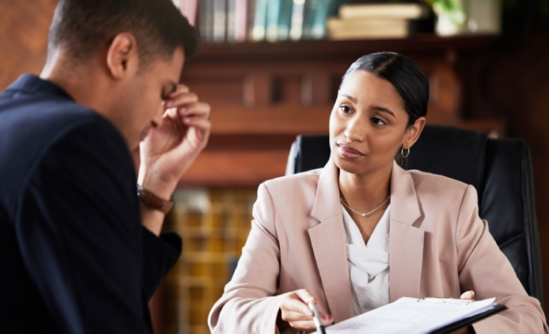 Female professional in a beige blazer consulting with a concerned male client in an office setting.